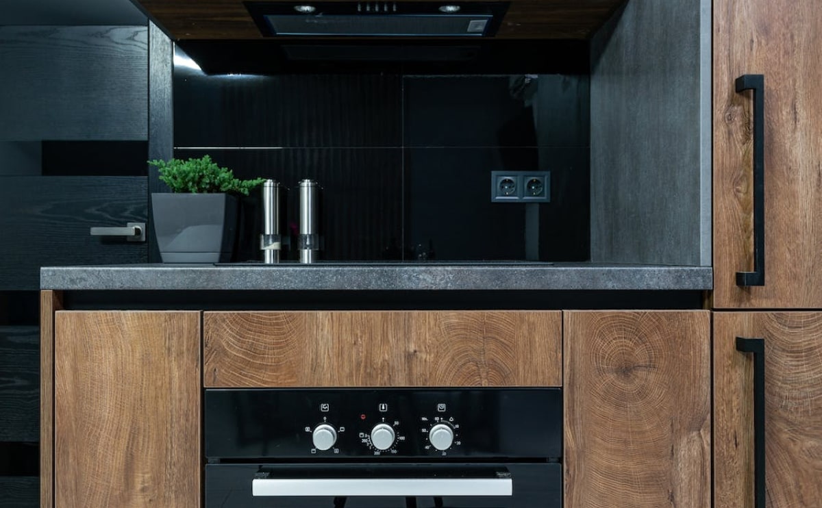 Modern kitchen with wooden cabinets and built-in oven with lighting.