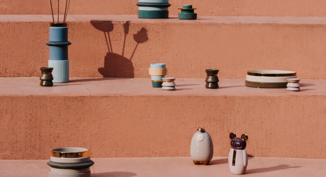 Decorative ceramic vases and figurines on terracotta stairs with shadows.