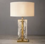 Elegant clear glass table lamp with brass accents and a white shade.