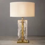 Elegant clear glass table lamp with brass accents and a white shade.