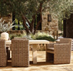 Outdoor patio with wicker chairs and stone building under trees.