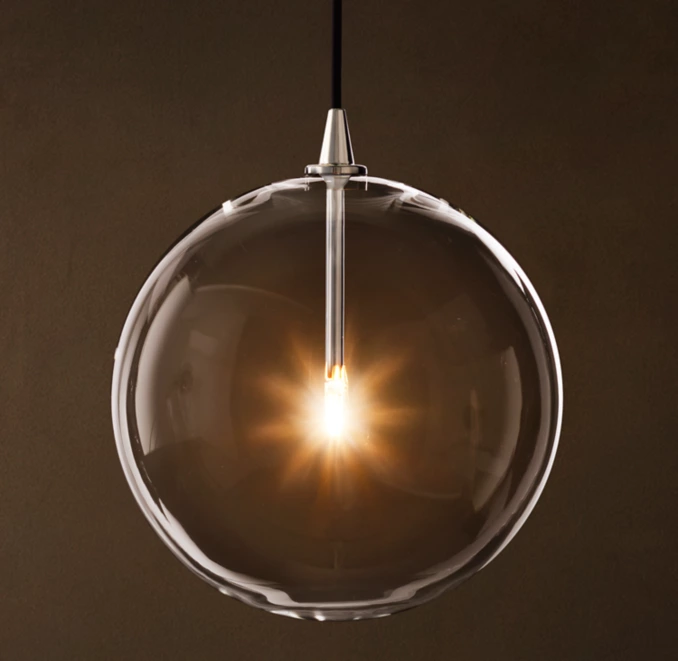 Elegant glass pendant light with warm glowing filament bulb.