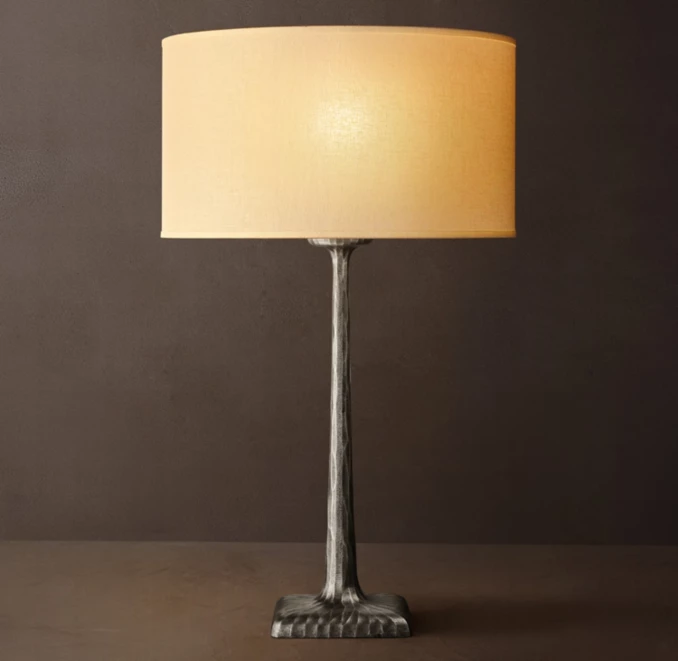 Forged metal lamp with beige lampshade on dark background.