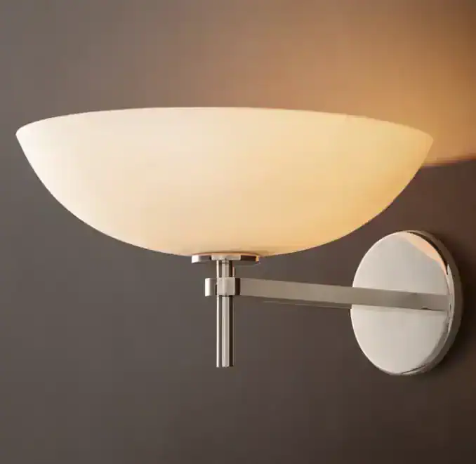Modern porcelain wall sconce with brass arm and round base, warm lighting.