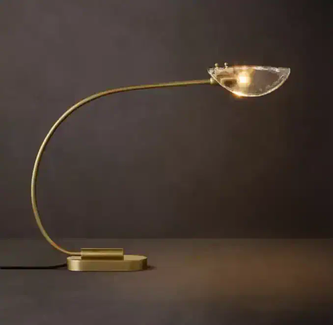 Modern table lamp with a curved brass arm and glass shade for ambient lighting.