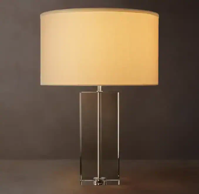 Modern crystal table lamp with beige fabric shade and metal base.