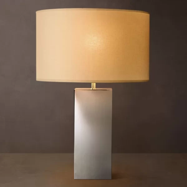 Modern brass square table lamp with beige lampshade on dark background.