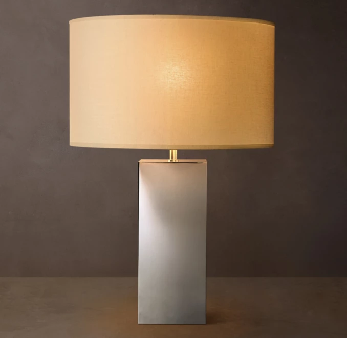 Modern brass square table lamp with beige lampshade on dark background.