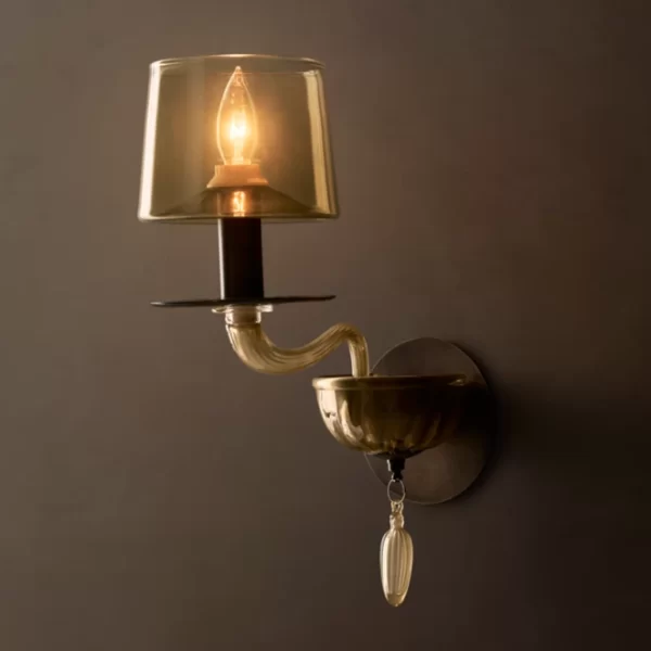 Elegant wall sconce with glass shade and decorative hanging element.
